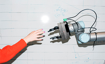 Et foto af en menneskearm og en robotarm, som rækker fingrene frem for at røre hinanden