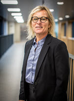 Portræt af en person med briller og mørk blazer i en indendørs gang.
