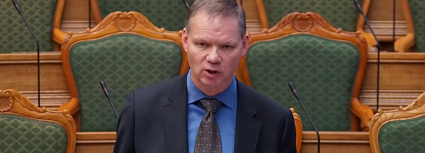 Jens_Henrik_Thulesen_Dahl speaking in a chamber with green upholstered seats and microphones behind him.