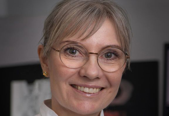 Close-up portrait of Malene Grubbe Hildebrandt smiling, wearing round glasses.