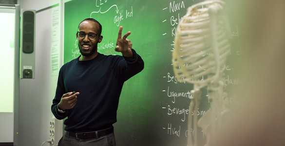 Picture of teacher in front of black board with a skeleton in the foreground.