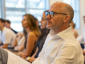 Deltagere til et arrangement sidder, lytter og kigger ligefrem. 