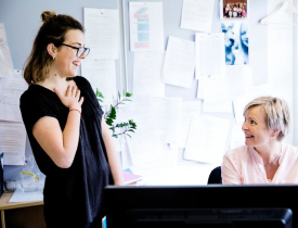 To kvinder har en samtale, hvor begge smiler eller griner.