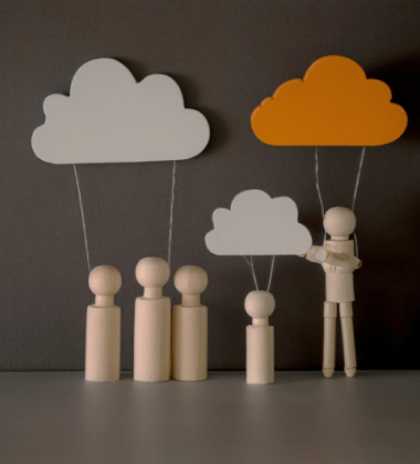 Træfigurer står under skyer af papir på snore; én figur holder en mindre sky, mens en anden større sky er orange og skiller sig ud.